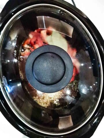 Lid placed on top of a Breville slow cooker full of slow cooker rump steak and onions