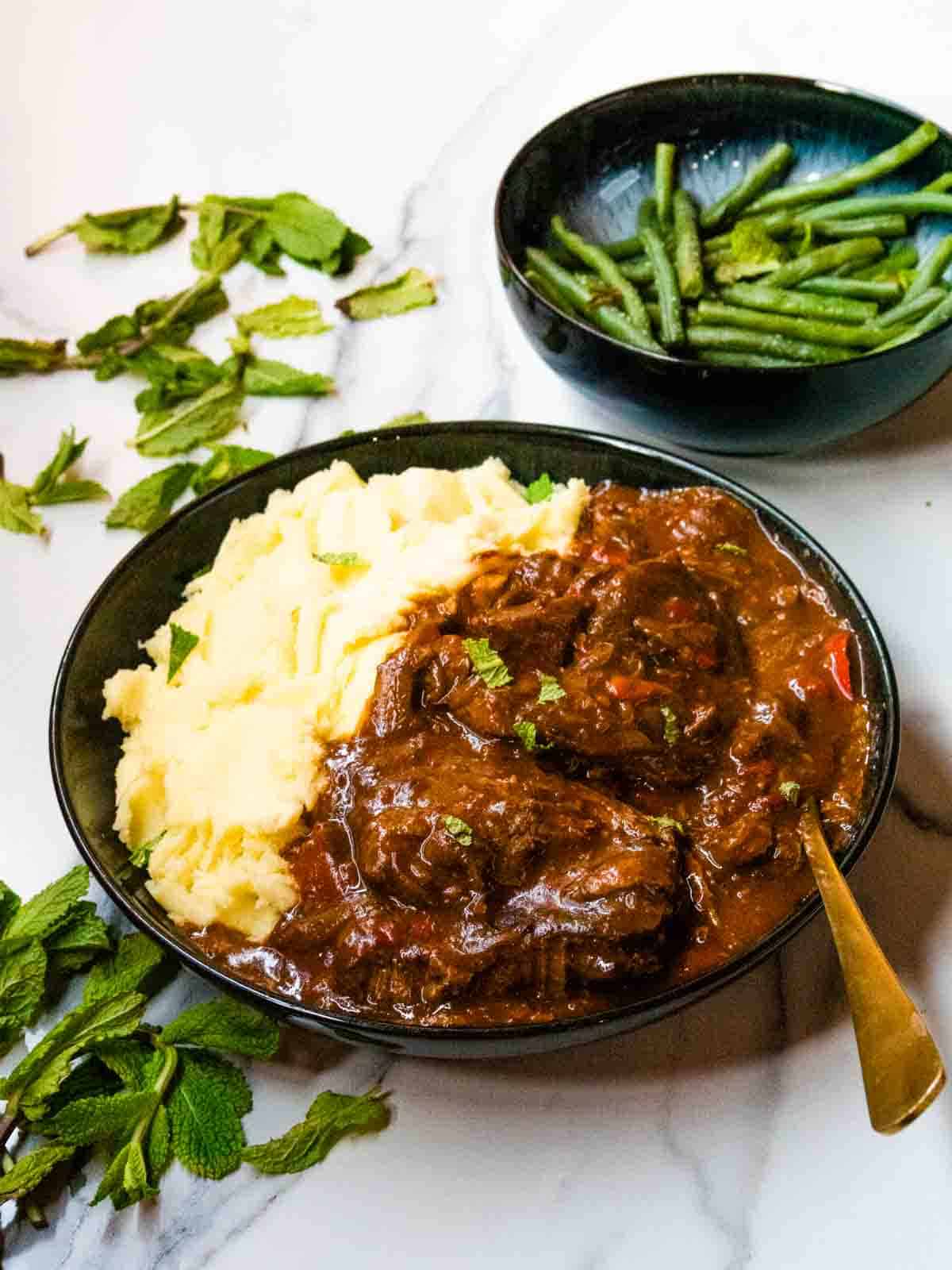 Angled photos of steak, red pepper onion gravy and mashed potatoes with green beans and fresh herbs on a marble kitchen counter