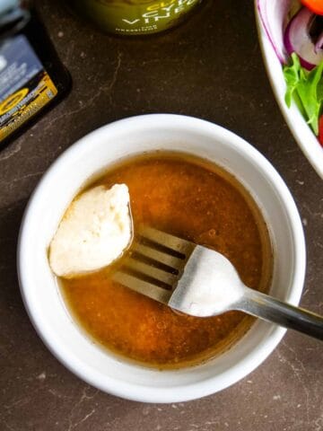 person mixing hummus into mackerel oil and other salad dressings in a ramekin dish
