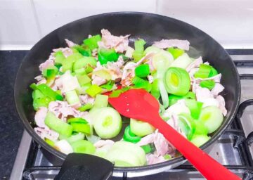 person frynig and sauteeing leeks in oil in a large frying pan