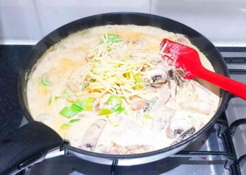 person making a homemade cheese sauce in a frying pan with double cream, cheese, milk and water until thickened