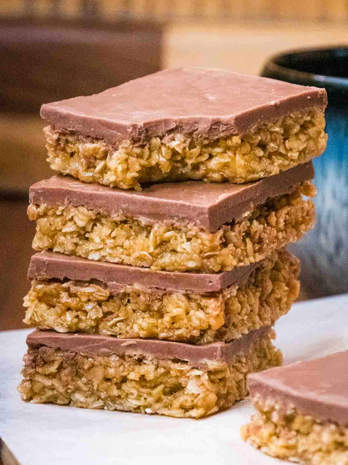 close up of a stack of chocolate flapjacks in front of a cup of tea and one with a bite mark