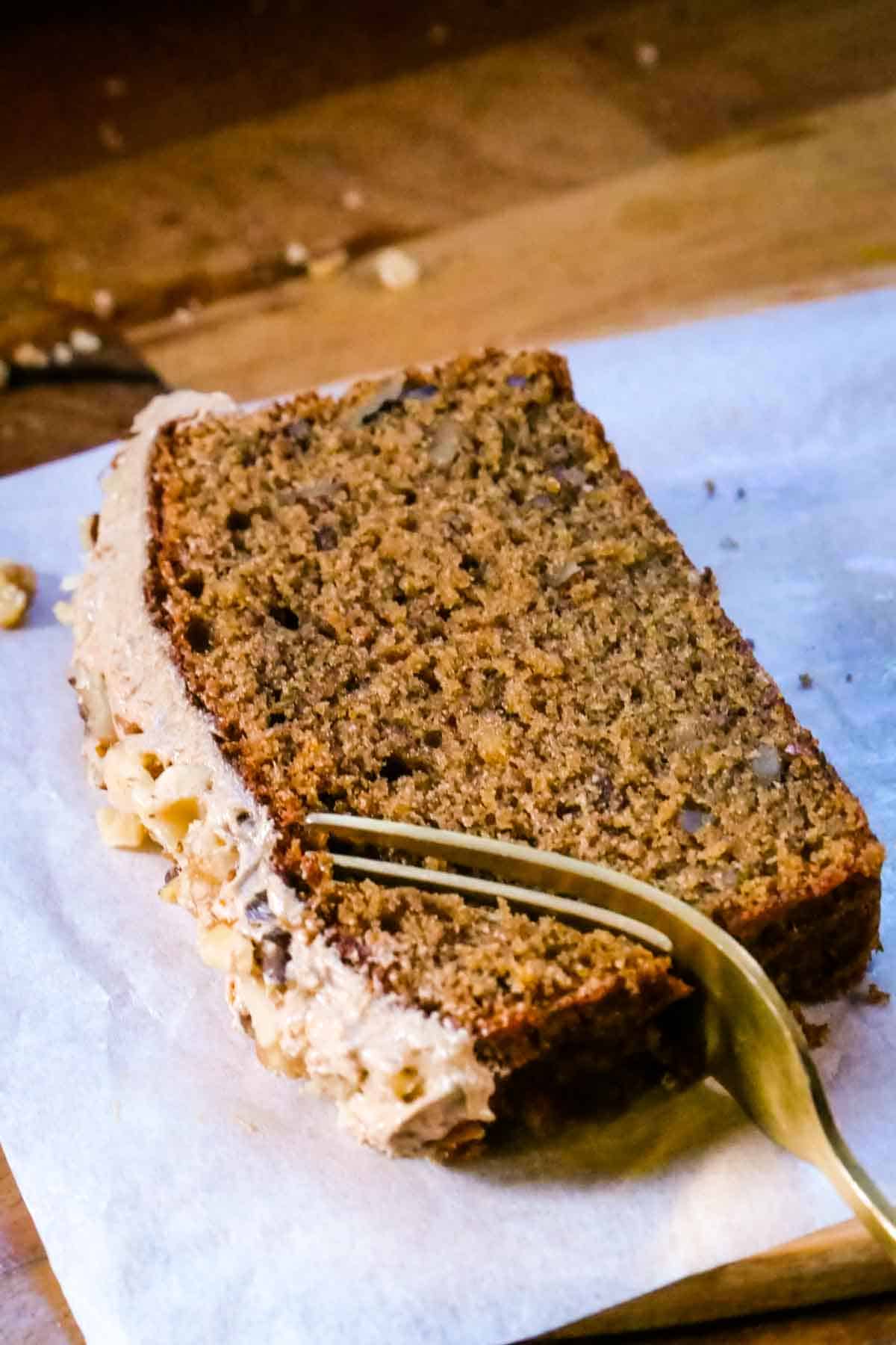 Person eating a slice of coffee and walnut cake recipe with a gold fork