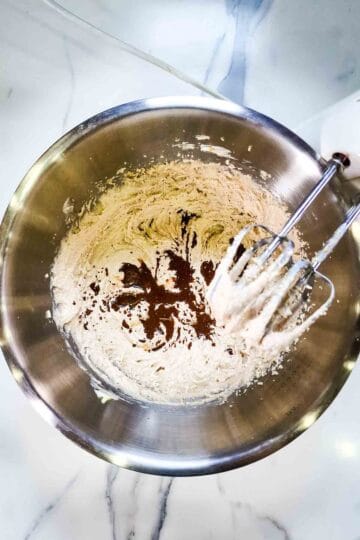 person mixing coffee extract into a cake batter with a hand mixer in large bowl