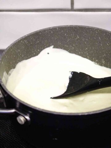 person making an easy bechamel sauce by melting cream, cheese and nutmeg in a medium saucepan