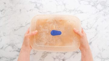 person shaking a tupperweare container full of potato chips, herbs and spices, shaking off excess oil