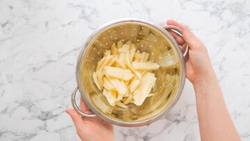 person draining washed potatoes in a colander