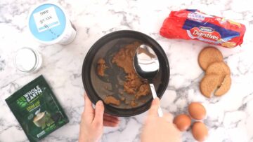 person pressing a cheesecake biscuit base in a buttered and lined cake tin
