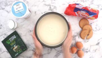person shaking a cake pan with cheesecake topping on biscuit crumb to level the top