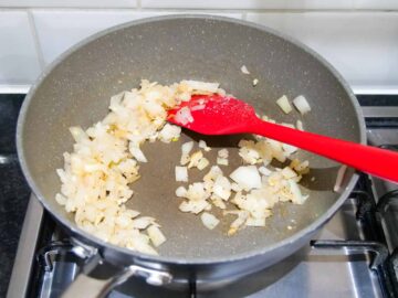 person frying onions and garlic in a large saute pan