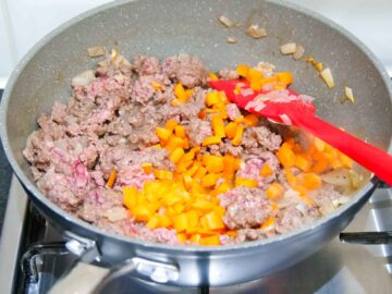 person browing beef at the same time as frying onions for a ragu