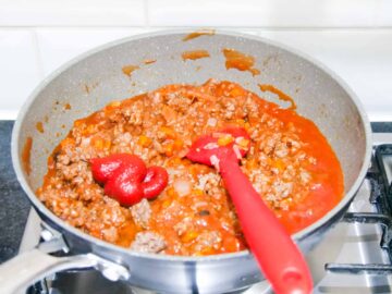 person making a red lasagne sauce in a pan with passata, tomato puree and beef mince