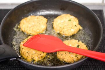 mackerel patties frying in a large pan in their own olive oil