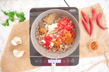 beef mince, peppers, garlic and onions in a large frying pan on electric induction hob cooking healthy chilli con carne