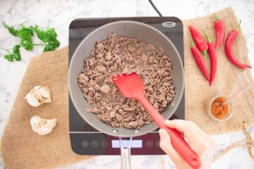 person browning minced beef in cooking oil spray in a large frying pan