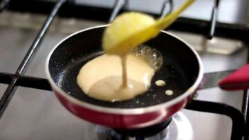 Person pouring a tablespoon of pancake batter into a mini frying pan oiled with Frylight cooking oil spray