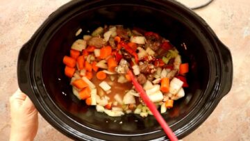 person stirring beef stew ingredients in a slow cooker before cooking