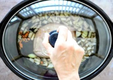 person placing a lid on top of a slow cooker with gammon and coke with vegetables before cooking