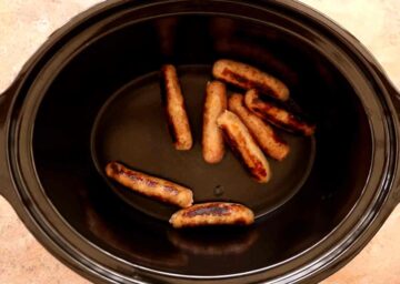 browned sausages in the bottom of a slow cooker