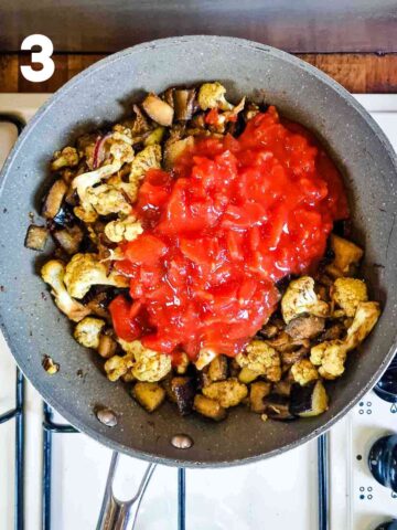 chopped tomatoes added to a pan for a tomato based vegan aubergine and cauliflower curry cooking on the stove top