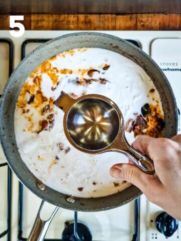 person drizzling lemon juice into a vegan vegetable curry with coconut milk