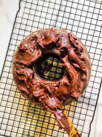Person spreading a quick birthday cake topping of Betty Crocker fudge chocolate icing sugar on a ring cake brownie recipe while on a wire rack