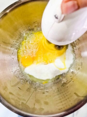 person whisking eggs and baking sugar in a large steel mixing bowl
