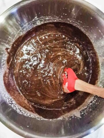 person folding chocolate sauce into eggs and sugar in a large mixing bowl