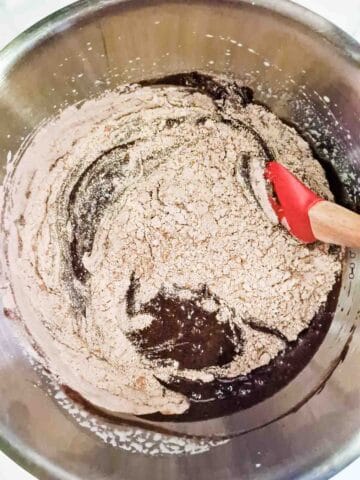 person folding flour and cocoa powder into dark chocolate mixture