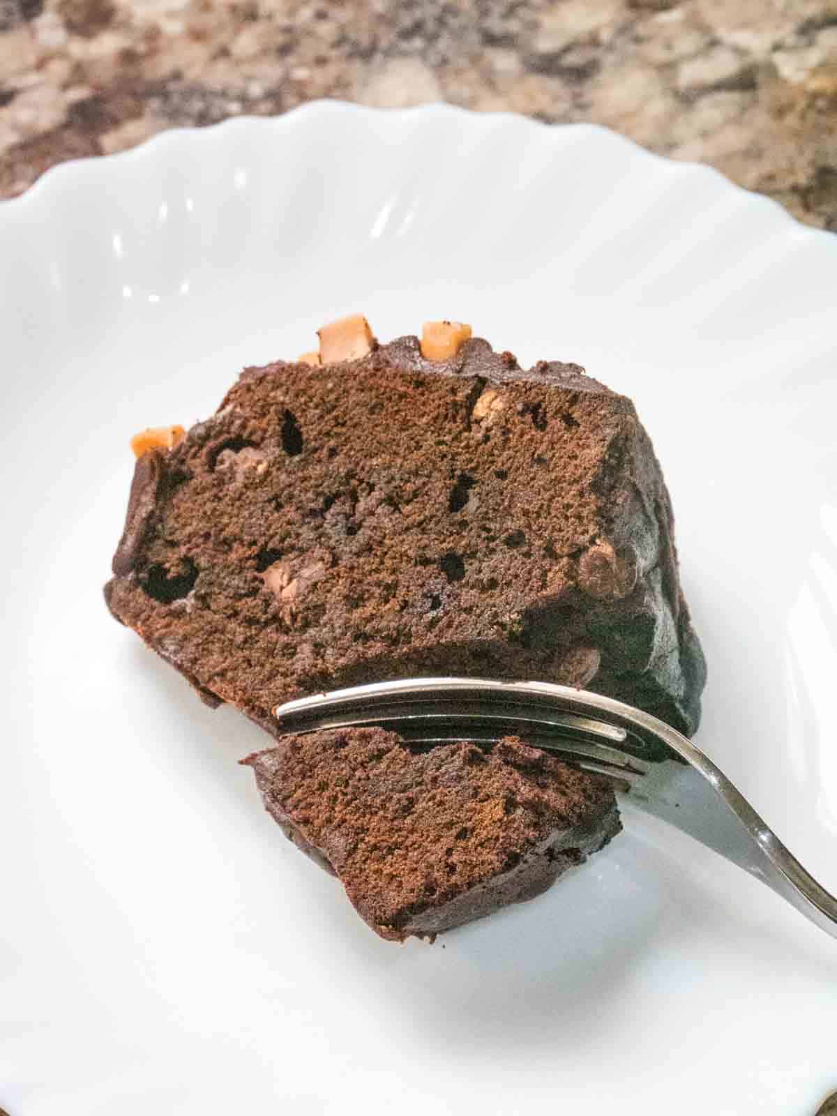Person cutting up a slice of chocolate donut birthday cake with a fork on a white plate