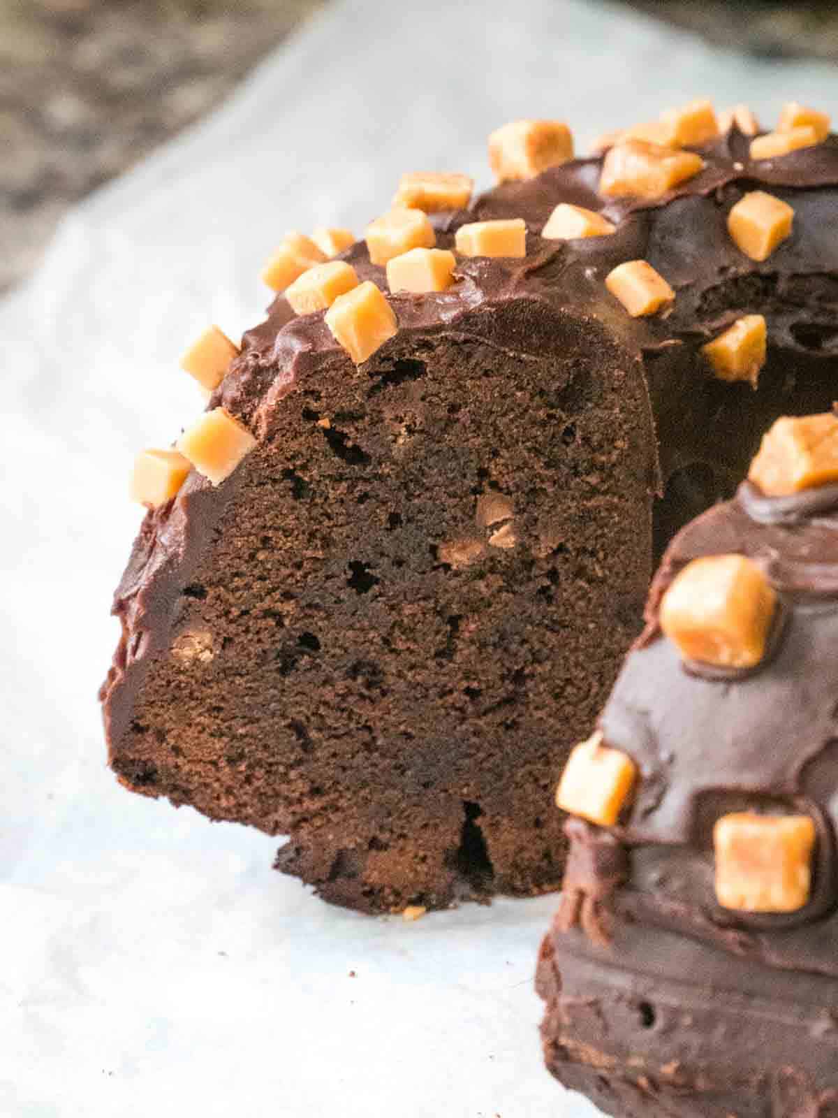 Close up of a sliced chocolatey birthday ring cake on baking paper and fudge crown topping
