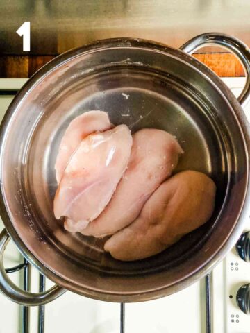 chicken breasts being poached in a deep pan of cold water on the hob