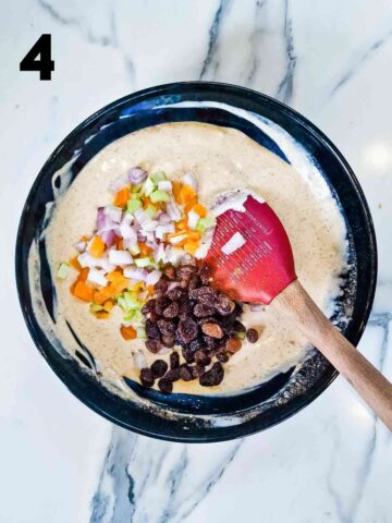 person stirring dried sultanas, apricots, celery and shallots into a curried mayonnaise and Greek yogurt sauce for King Charles III coronation