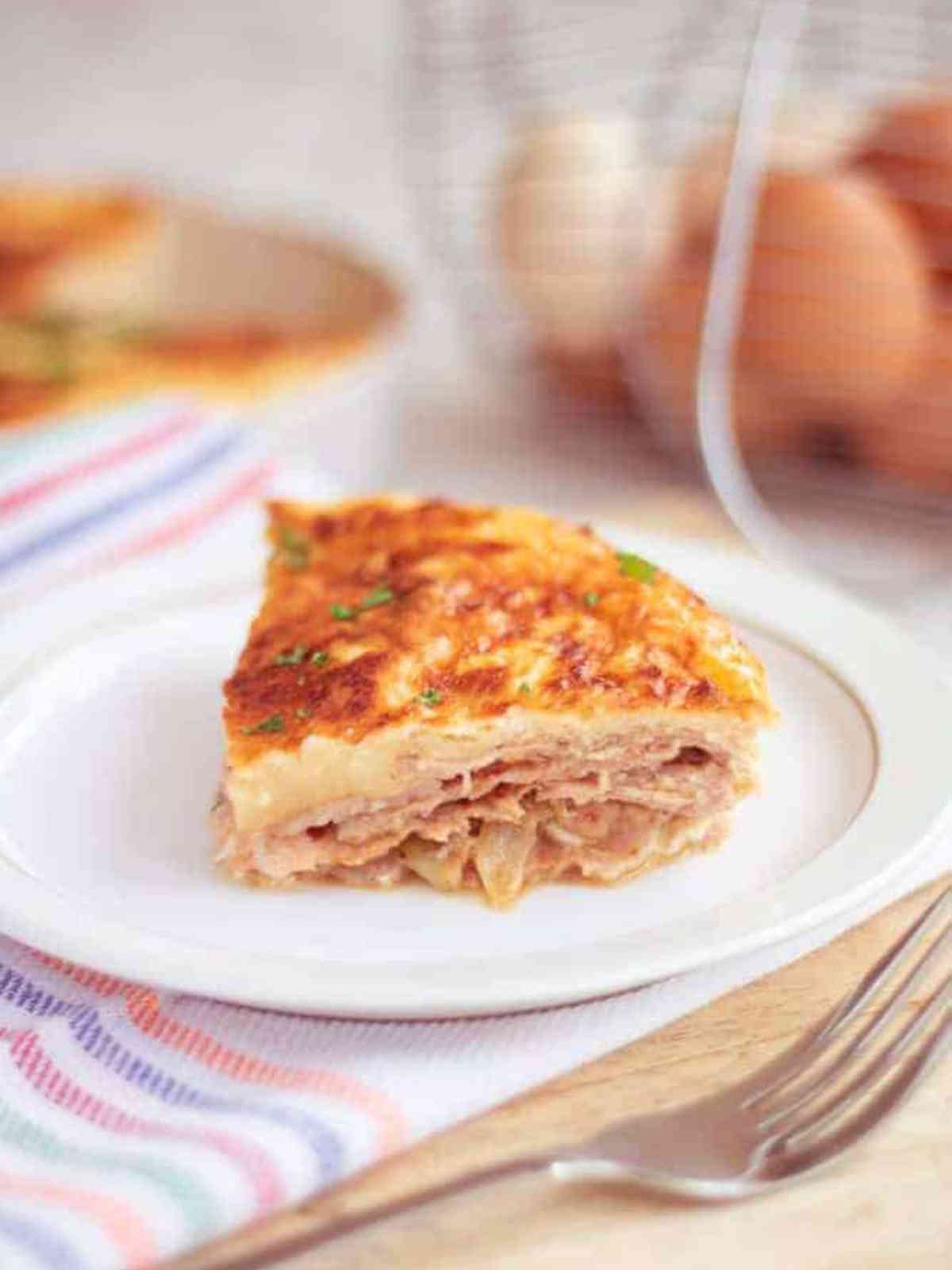 Close up of a slice of bacon and egg pie on a white plate surrounded by aeggs in a chicken basket