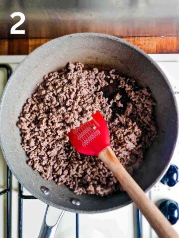 person browning ground beef with a wooden spoon in a pan