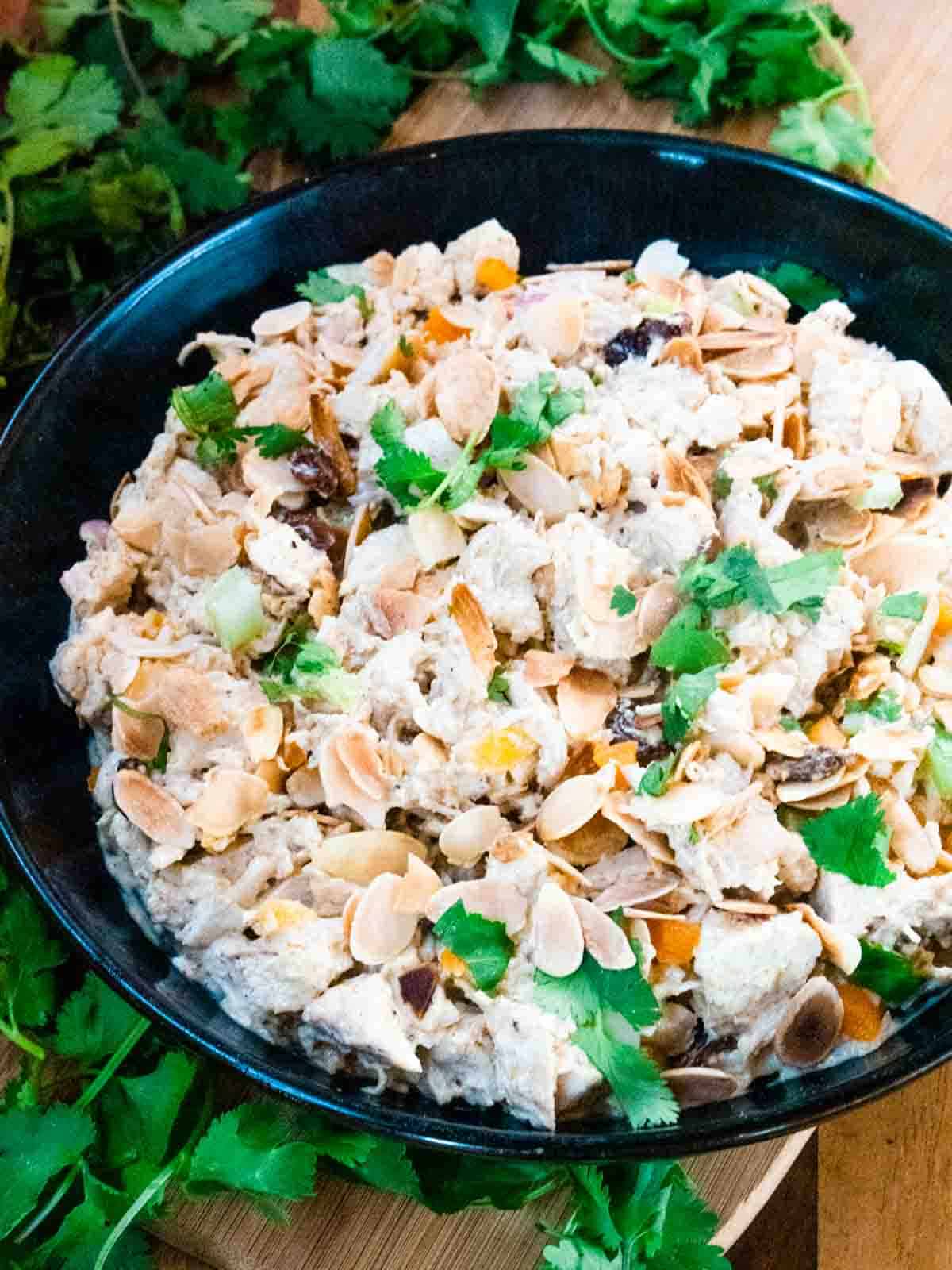 close up of a large black bowl full of Coronation chicken mixture topped with toasted almonds, celery and fresh coriander