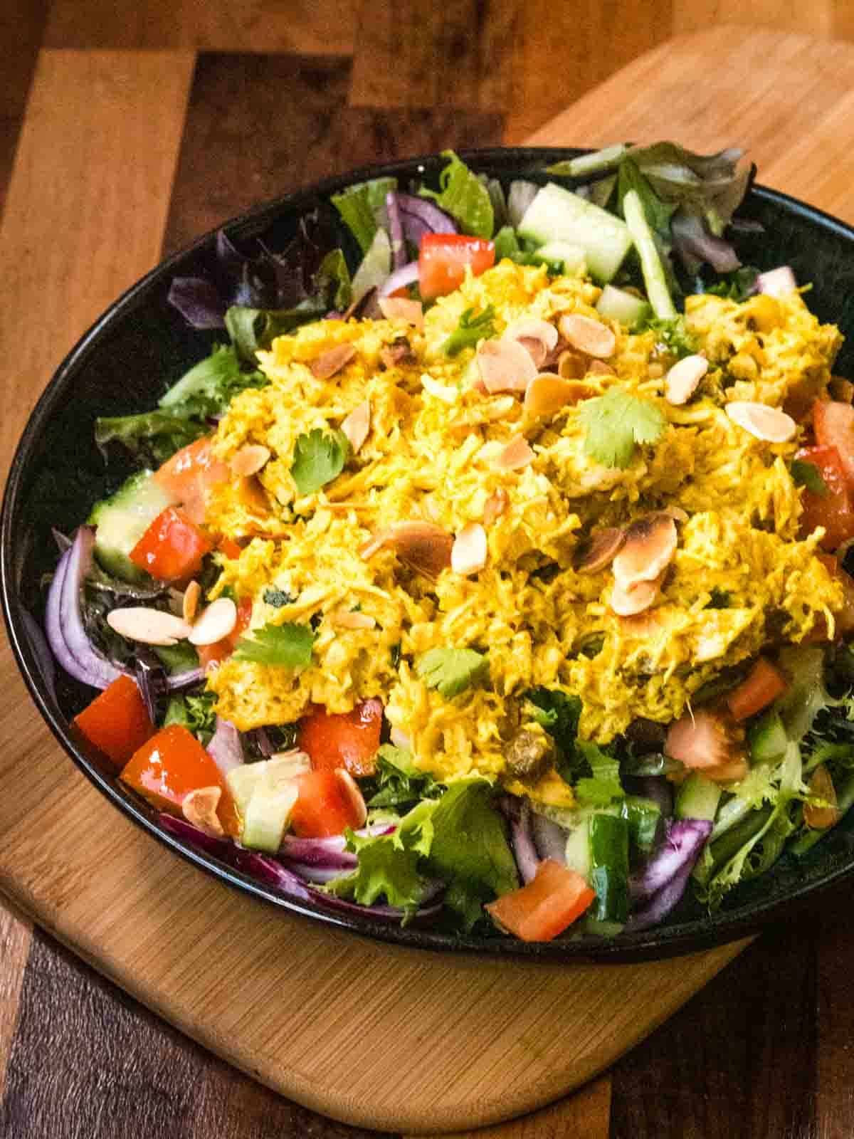 Shredded Coronation chicken on a chopped salad in large black Denby bowl on wooden kitchen worktop