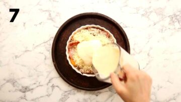 person pouring egg mixture on cheese, bacon and eggs in quiche dish