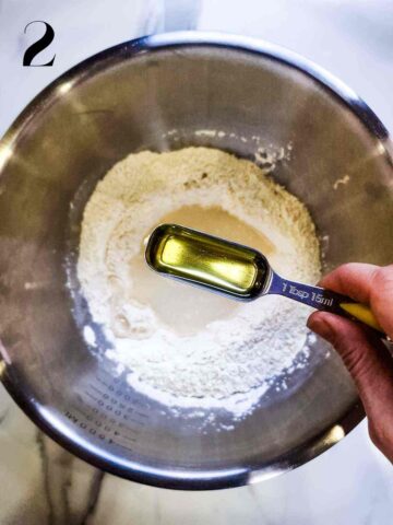 a well in the center of dry pizza dough ingredients with water and oil being poured in