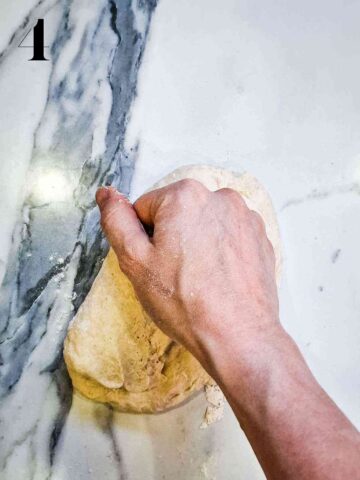 person kneading pizza dough on a well floured marble kitchen worktop
