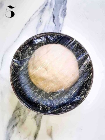 dough proofing in an small black oiled bowl covered in clingfilm