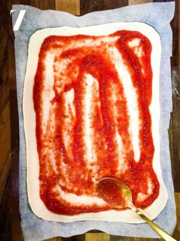 person spreading marinara sauce on pizza dough on baking paper