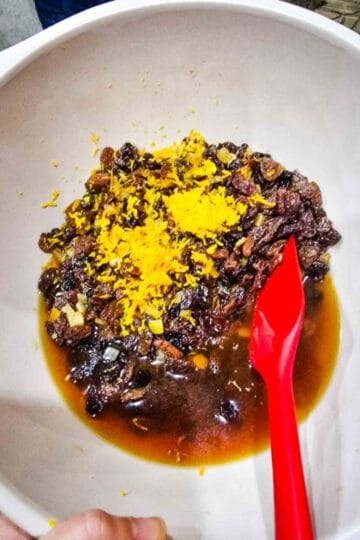 mixing black tea, hot water, dried fruit, and citrus peel in a mixing large bowl