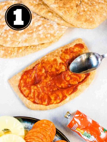 person spreading tomato puree on wholemeal pitta bread