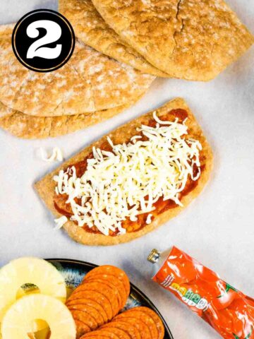 grated cheese on pita bread with tomato puree surrounded by toppings