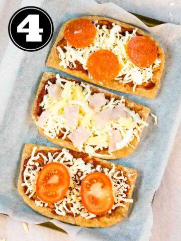 3 pitta pizzas on a lined baking tray before baking in the oven