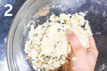 person mixing dried fruit into shortcrust dough by hand while in a glass mixing bowl