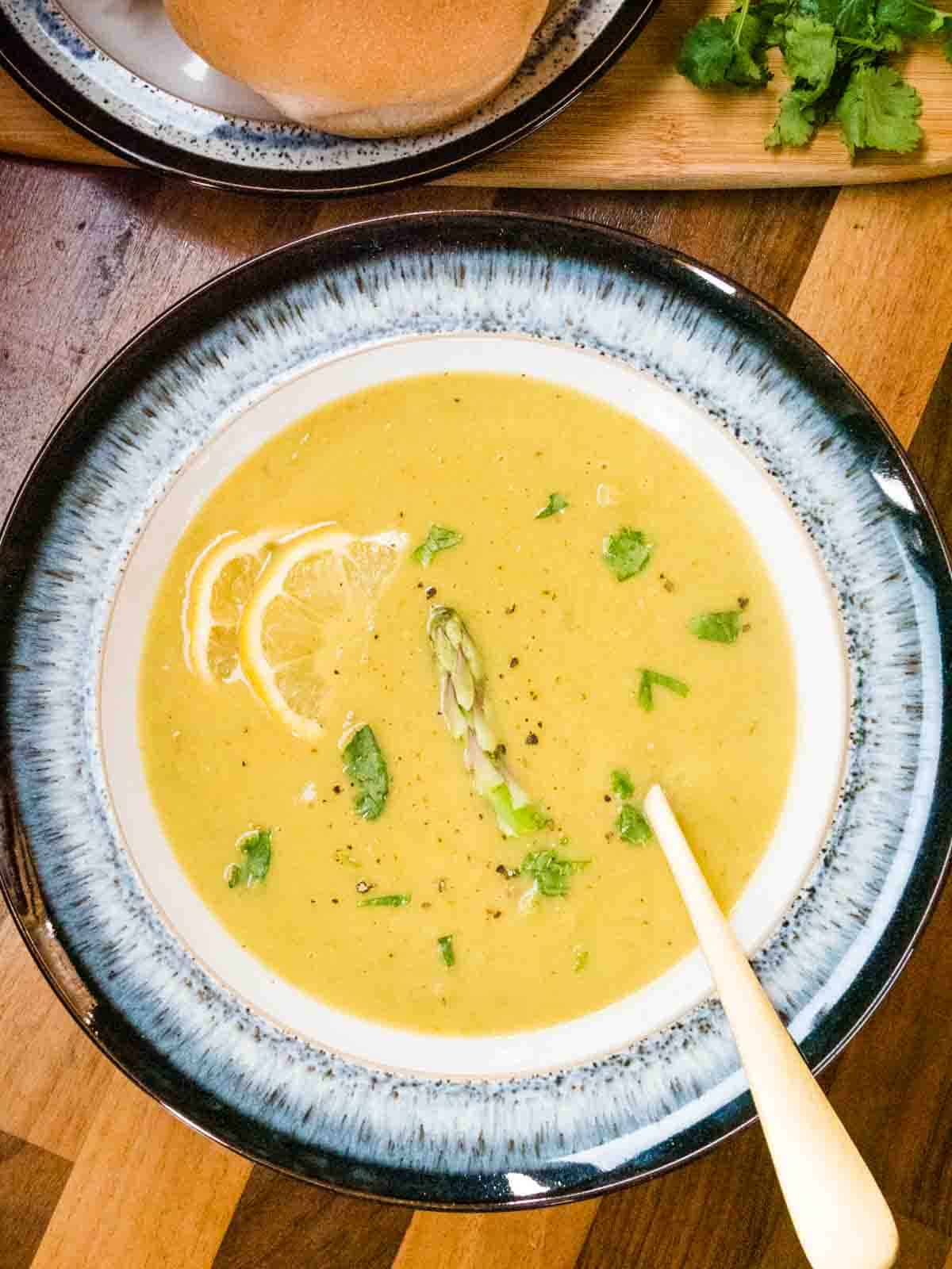 fresh asparagus soup in a black rimmed bowl with a single spear and coriander garnish on a wooden butcher block worktop