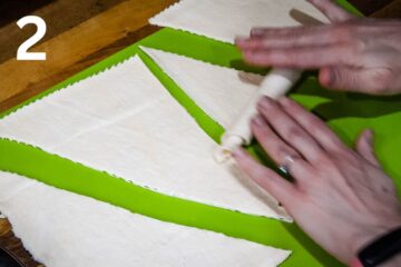 person rolling croissant pastry from the shortest side to the pointed end