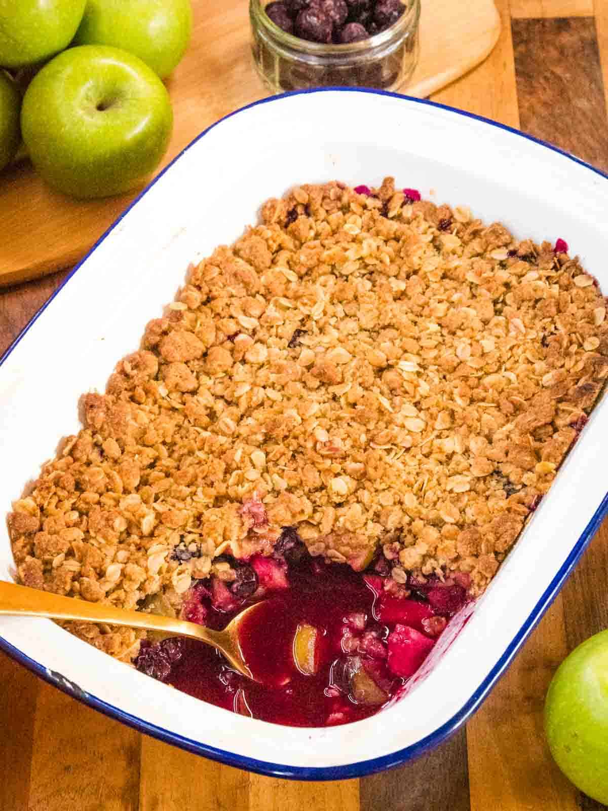 spoonful of apple blueberry crumble missing from a freshly baked crumble dessert on wooden kitchen worktop